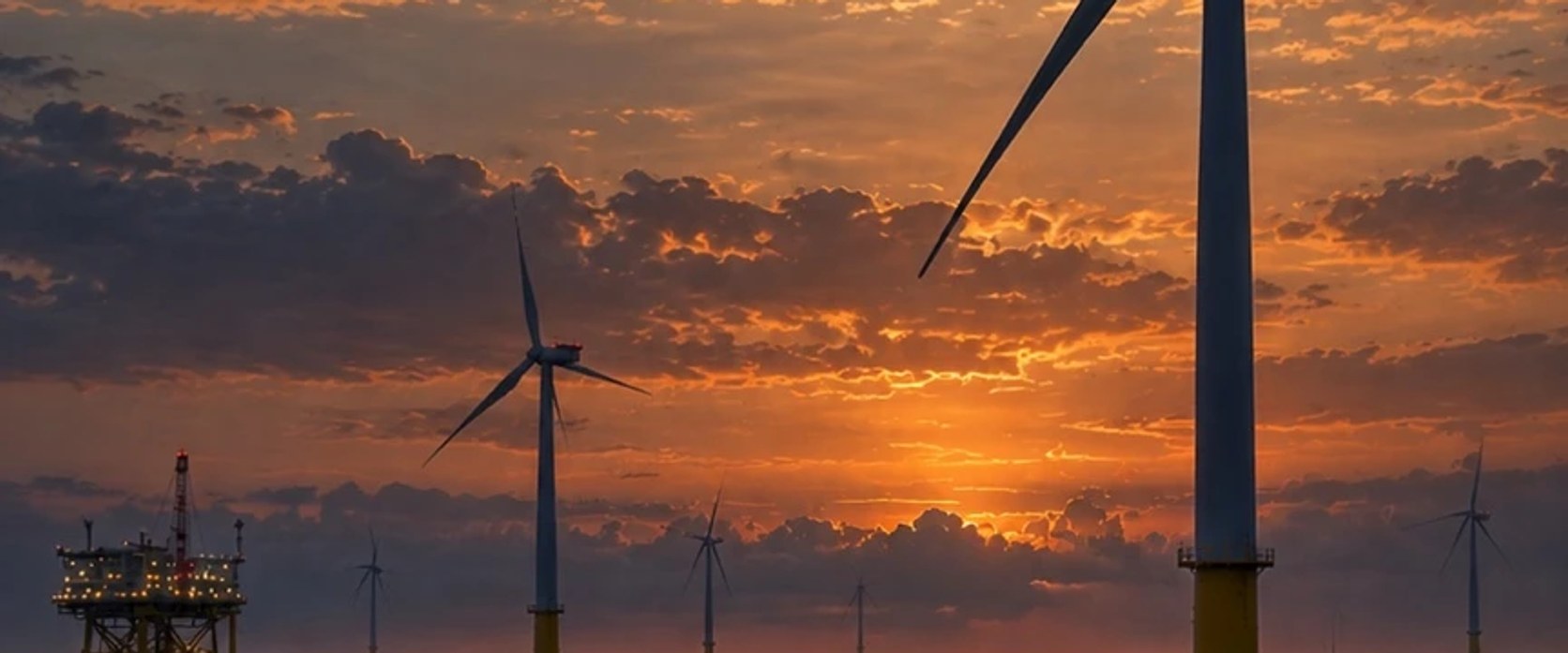 Offshore wind turbines silhouetted against a sunset, with a support platform in the distance